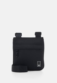 Svart nylon crossover-väska med en texturerad yta, justerbara remmar, framficka med dragkedja och kontrasterande logodetalj.