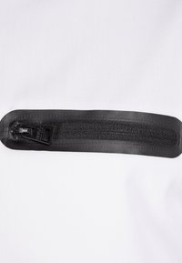 Schwarzer Reißverschluss mit einem strukturierten Ziehband, das an einem glatten weißen Stoffhintergrund befestigt ist, und mit einer versiegelten Kante für Langlebigkeit.