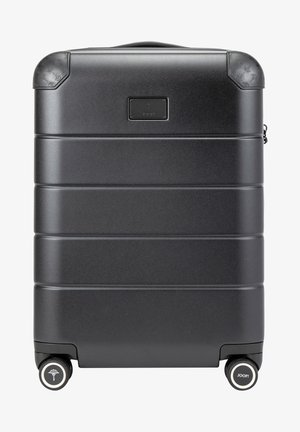 Črn trdi kovček s horizontalnimi rebrami, zaobljenimi koti in gumijastimi detajli. Ima dve kolesi in označbo blagovne znamke spredaj.
