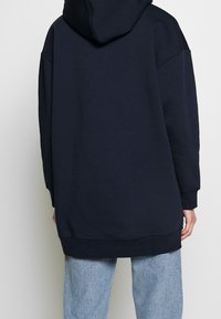 Sudadera amplia de color azul marino con capucha ajustable, mangas largas y dobladillo acanalado. Tejido suave con una textura lisa, sin patrones ni acentos.