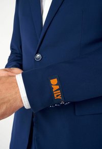 Jūrų laivyno švarkas su lygiu audiniu, vieno mygtuko užsegimu ir oranžine "DAILY" etikete ant rankovės. Pasižymi pritaikytu siluetu ir subtiliais siuvinėjimais.