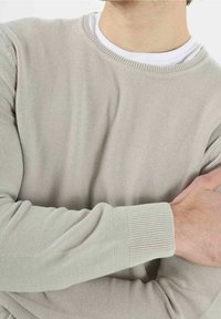 Jasnoszary, dziany sweter z okrągłym dekoltem, ściągaczami przy mankietach i teksturowanym materiałem, częściowo pokazany na osobie z założonymi rękami.