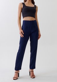 Tmavě modré kalhoty na míru s vysokým pasem, zdobené sklady a hladkou texturou, v kombinaci s černým zkráceným topem.