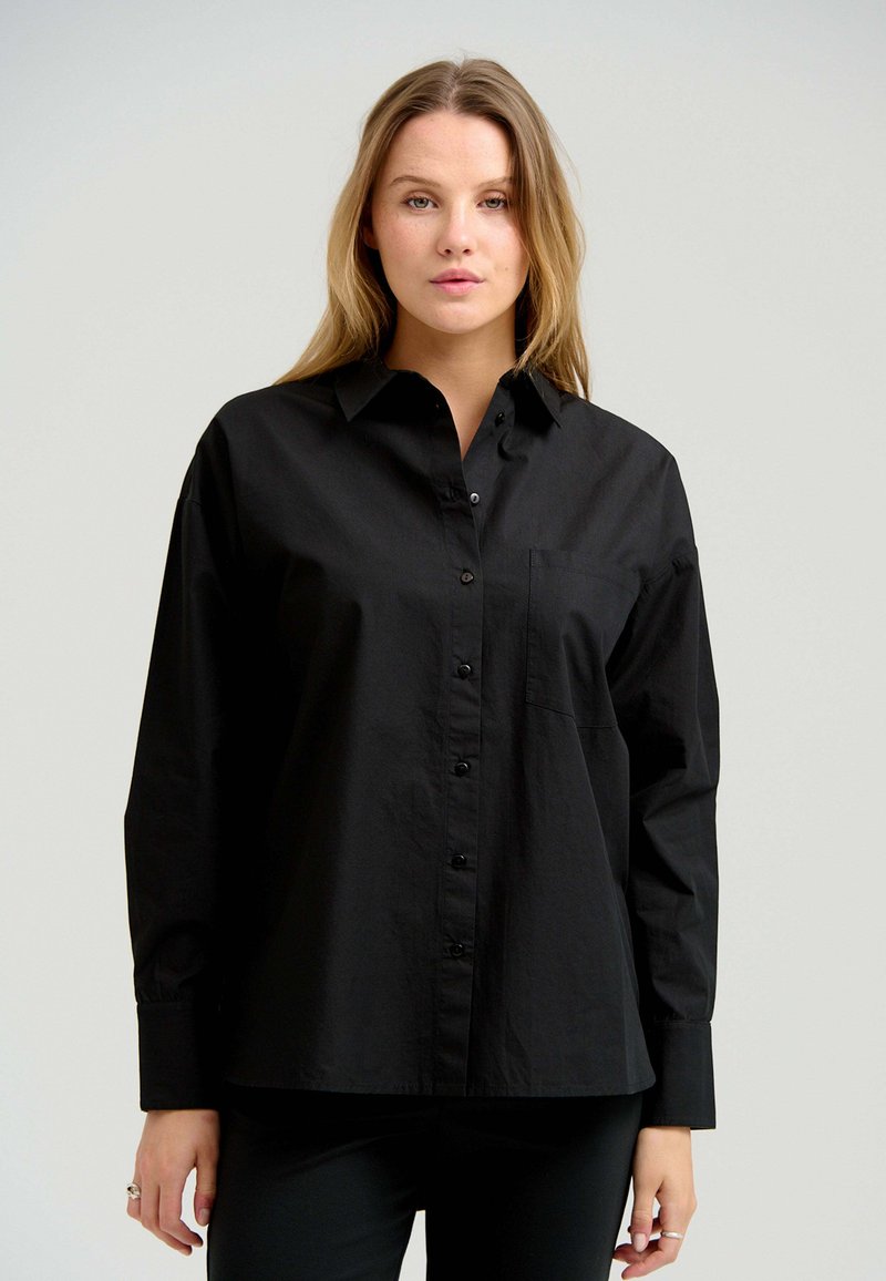 Sort skjorte med knaplukning lavet af glat stof, med en klassisk krave, lange ærmer og en brystlomme. Simpelt design uden mønstre.