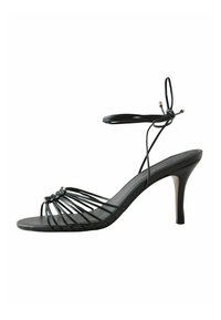 Sandale noire à talons hauts avec fines lanières autour de la cheville et un talon aiguille de hauteur moyenne sur fond blanc.