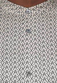 Κοντομάνικο πουκάμισο με λευκό και μαύρο γεωμετρικό σχέδιο, με γιακά μαανδάριν και γκρι κουμπιά, που αναδεικνύει ένα υφασμάτινο σχέδιο.