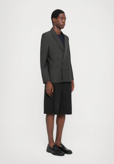 Γκρίζα διπλή ζακέτα με πέτο, σε συνδυασμό με μαύρες βερμούδες μέχρι το γόνατο και μαύρα μπαραίνα. Λείο ς υφασμάτινος ιστός.