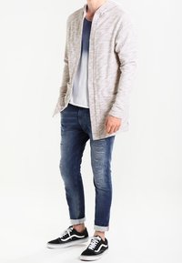 Ljusgrå, texturerad cardigan med huva, buren över en blå ombre-t-shirt, kombinerad med slitna mörka jeans och svarta sneakers.