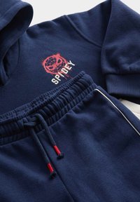 Sada tmavě modré mikiny a tepláků, která obsahuje grafiku červené pavučiny a bílé písmo "SPIDEY". Elastický pas s červenými šňůrkami.