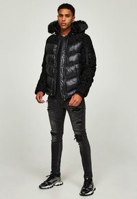 Black puffer jacket with a fur-lined hood, featuring a quilted design and metallic accents. Paired with ripped black jeans and sporty sneakers.