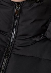 Close-up of black quilted jacket with visible metal zipper partially zipped up.