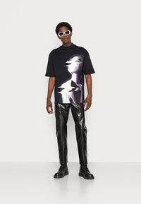 Black oversized t-shirt with a purple and white abstract print, paired with shiny black leather pants and black lace-up boots. White sunglasses.