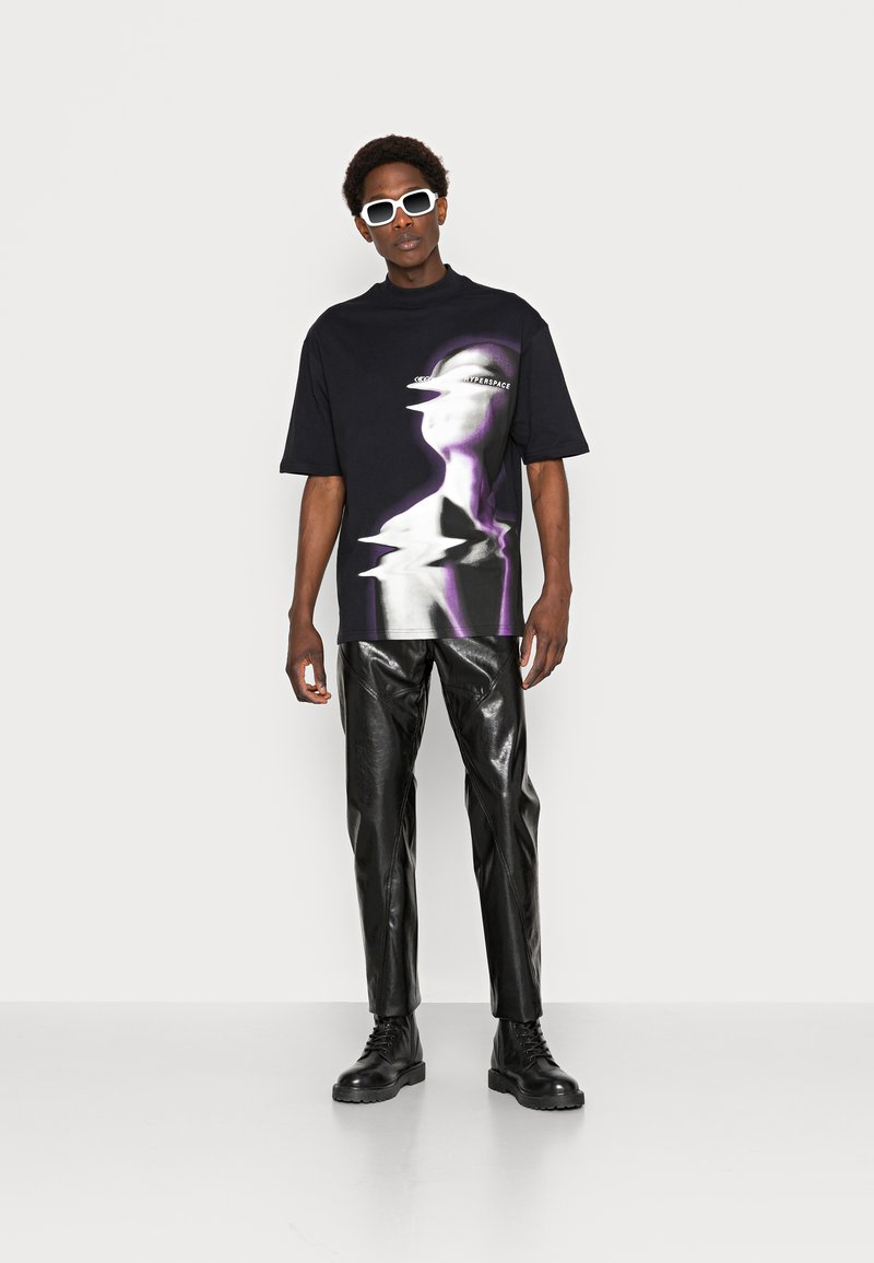 Black oversized t-shirt with a purple and white abstract print, paired with shiny black leather pants and black lace-up boots. White sunglasses.
