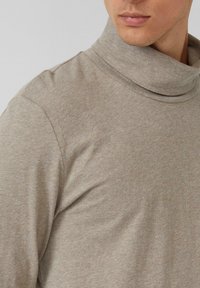 Beżowy sweter z golfem wykonany z miękkiej dzianiny. Ma luźny krój i złożony kołnierz dla dodatkowego komfortu. Tekstura wydaje się gładka.