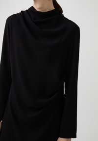 Zwarte jurk met lange mouwen, voorzien van een gedrapeerde halslijn en een soepele textuur, gemaakt van een zacht materiaal. Minimalistisch ontwerp zonder opvallende accenten.