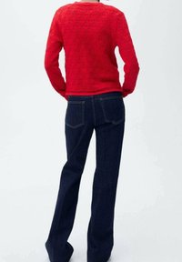 Rød strikket sweater med et struktureret mønster og en cropped kant, parret med mørkeblå flare jeans med standardlommer og syninger.