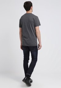 Szara koszulka krótki rękaw, bawełniany materiał, luźny krój, w połączeniu z ciemnoniebieskimi dżinsami i czarnymi botkami za kostkę, widok z tyłu.