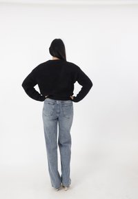 Suéter negro de punto con cuello redondo, combinado con unos jeans de tiro alto y pierna recta en azul claro que cuentan con bolsillos traseros y un corte clásico.
