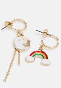 Brincos em aro dourados com pendentes: um apresenta um design circular de yin-yang com um detalhe em cristal, o outro um arco-íris colorido com detalhes em nuvem.