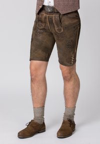 Ruskeat nahka-lederhosenit, joissa on koristeellista brodeerausta, sivunapit ja kaksi taskua. Yhdistetty ruskeisiin kenkiin ja harmaisiin sukkiin.