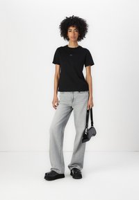 Svart t-skjorte med korte ermer, lett stoff, avslappet passform, kombinert med høytlivede grå jeans, kraftige svarte plattform sko og en liten svart veske.