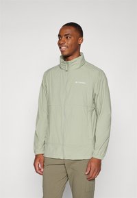 Light green zip-up jacket with a high collar and elastic cuffs, featuring a logo on the left chest and a lightweight, textured fabric.