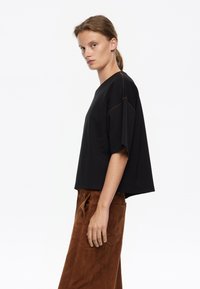 Čierny oversized krátky rukáv top s okrúhlym výstrihom a kontrastným hnedým stehom, v kombinácii s hnedými semišovými nohavicami s širokými nohavicami.