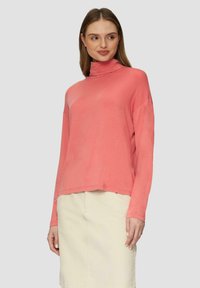 Korallenfarbener Langarmrollkragenpullover aus einem weichen, leichten Stoff, mit einem entspannten Schnitt und geradem Saum, kombiniert mit einem hellen Rock.