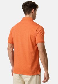 Polo à manches courtes en tissu orange chiné, présentant un col classique et une coupe structurée avec des fentes sur les côtés pour plus de liberté de mouvement.