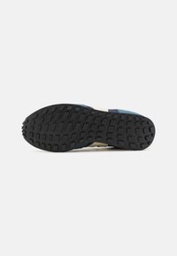 Shoe outsole featuring a black rubber sole with a textured pattern, and blue and cream accents in the upper material.