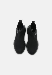 Black ankle boots featuring a knitted upper, elastic sides, and a textured surface. Sole has a smooth design, with logo detail on the inside.