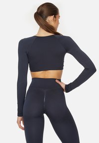 Navyblauer Langarm-Crop-Top mit nahtlosem Design und engen Bündchen, kombiniert mit hoch taillierten Leggings mit strukturiertem Muster.