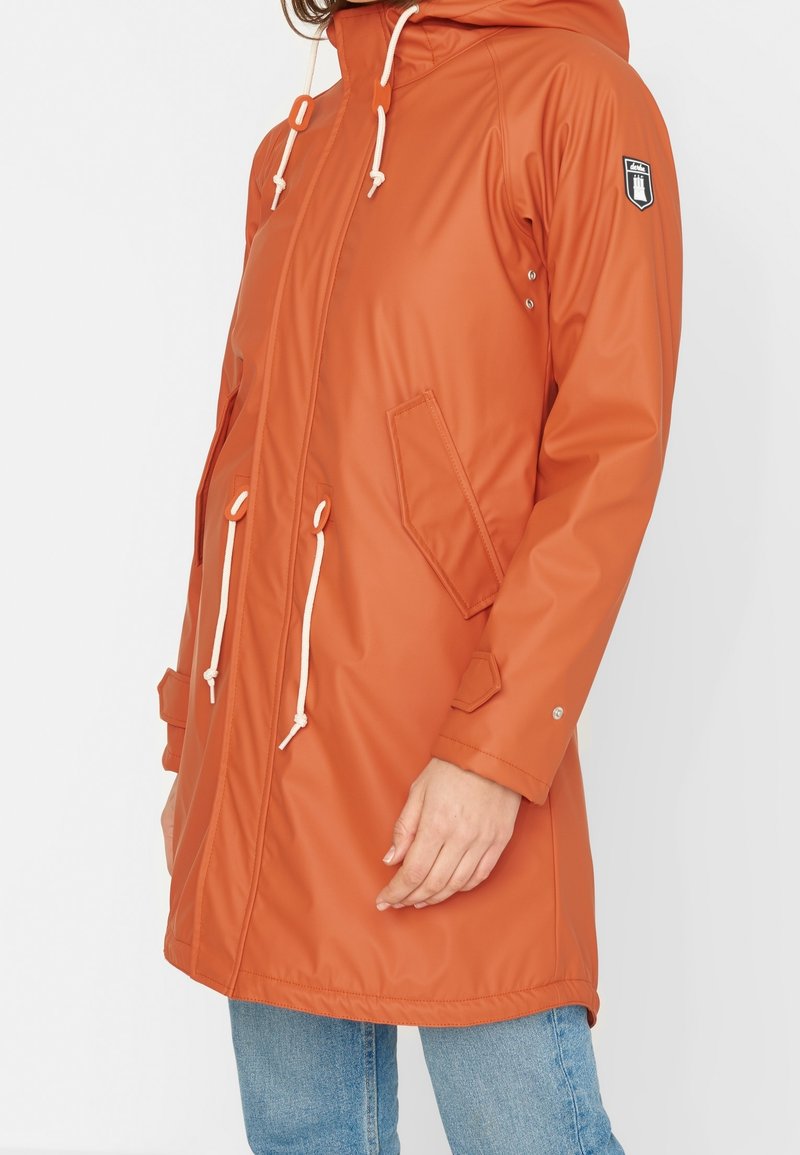Parka orange résistant à l'eau avec capuche, fermeture à cordon, deux poches latérales et accents blancs contrastants. Texture douce et lisse.