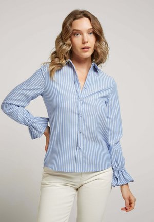 Chemise bleu clair à boutons avec des rayures verticales blanches, dotée d'un col et de poignets froncés. Fabriquée dans un tissu lisse.