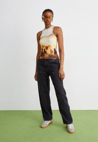 White sleeveless top with a gradient design featuring silhouettes of horses, paired with dark wide-leg pants and silver sneakers.