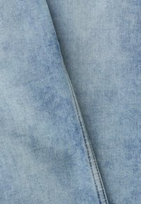 Tissu en denim bleu clair avec une couture diagonale visible courant verticalement au centre de l'image.