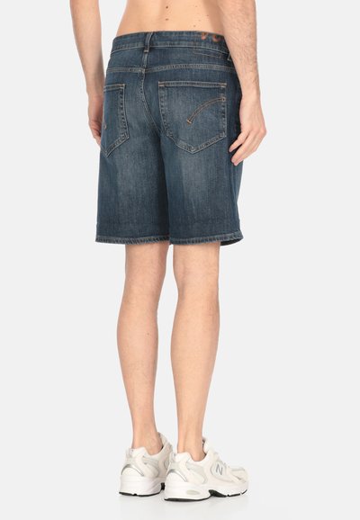 Pantalones cortos de mezclilla en azul oscuro con un dobladillo sin terminar, que cuentan con dos bolsillos traseros y costuras en contraste. Llevados con zapatillas deportivas blancas.