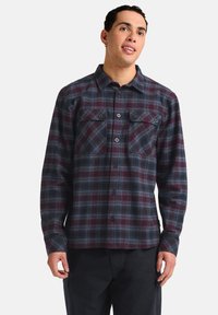 Chemise en flanelle à carreaux dans les tons bordeaux et marine, avec deux poches poitrine, fermeture à boutons et manches longues au fit décontracté.