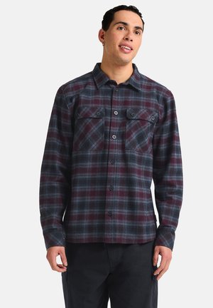 Chemise en flanelle à carreaux dans les tons bordeaux et marine, avec deux poches poitrine, fermeture à boutons et manches longues au fit décontracté.