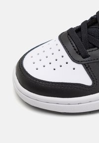 Svart och vit sneaker med en slät läderöverdel, perforerad vit tåbox, svarta snören och en strukturerad gummisula.