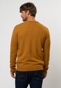 Senfgelbes Strickpullover mit gerippter Textur, langen Ärmeln und rundem Ausschnitt, kombiniert mit dunkelblauen Jeans.