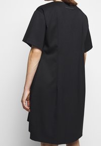 Vestido negro de manga corta, hecho de una tela suave, con un corte relajado, detalle de pliegue en la parte trasera y un diseño minimalista sin patrones visibles.