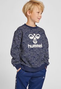 Sweatshirt bleu marine avec un motif de logo blanc répété, doté d'un col rond et de poignets côtelés. Tissu doux et coupe décontractée.