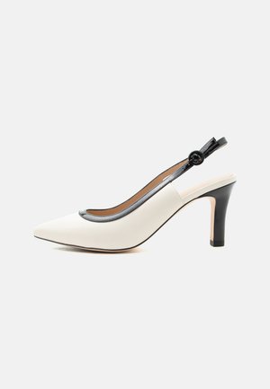 Witte puntige slingback pumps met hoge hak, zwarte afwerking en gesp op een effen achtergrond.