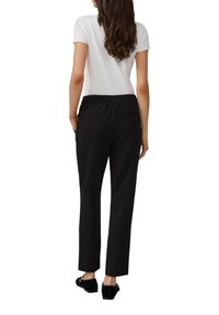 Pantalons noirs à coupe décontractée, avec une taille élastique et des poches arrière, associés à un haut blanc à manches courtes, vus de derrière.