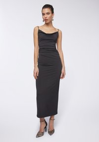 Abito nero aderente con spalline sottili, scollo a cowl e lati arricciati. Abbinato a scarpe con tacco alto in stampa leopardata.