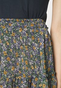 Zone de la taille d'une jupe fleurie avec de petites fleurs orange, violettes et blanches, associée à un haut noir ; ceinture élastique visible.