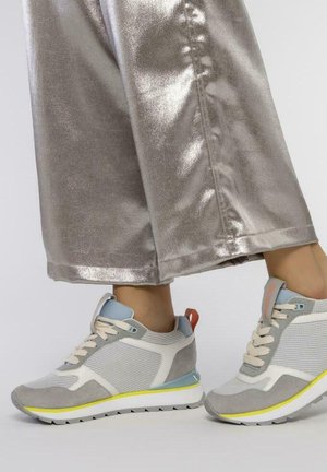 Baskets de sport grises avec des panneaux en mesh, accents bleu clair et semelle jaune. Portées avec un pantalon large argenté brillant.