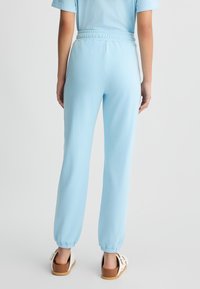 Pantaloni tuta azzurri chiari con vita ed elastici alle caviglie. Tessuto morbido, vestibilità comoda, abbinati a scarpe slip-on marrone chiaro.