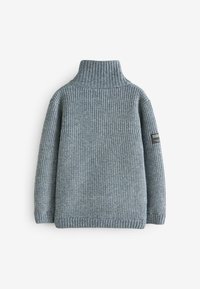 Gestrickter grauer Pullover mit hohem Kragen, der über eine gerippte Textur, überschnittene Schultern und ein schwarzes Markenlabel an einem linken Ärmel verfügt.